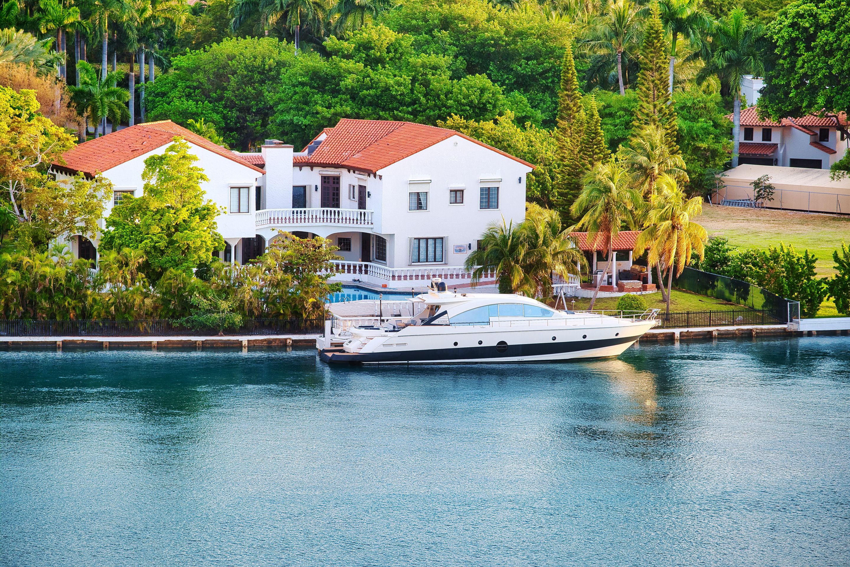 A waterfront home with a tile roof, a swimming pool and a boat at its dock