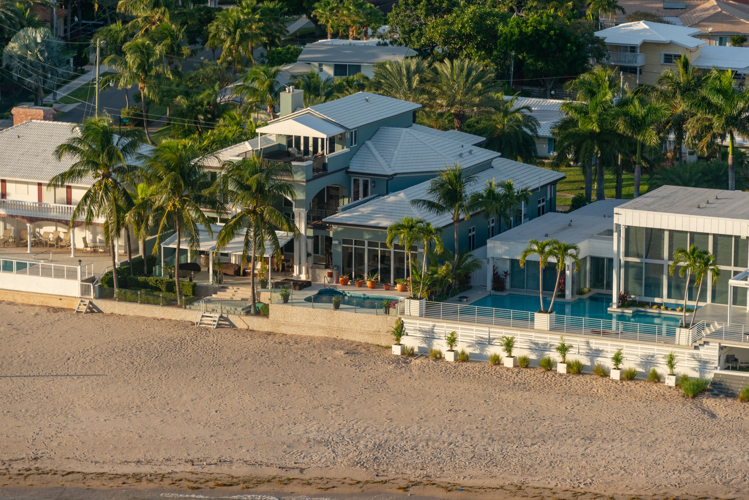 Beachfront homes with swimming pools and coconut palms at golden hour